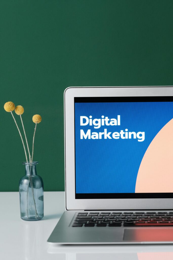 A laptop displaying 'Freelance Digital Marketing agency' with a minimalist floral decor in a glass vase.